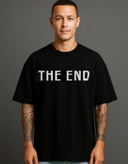 Man wearing black ATRAYE streetwear T-shirt with bold 'THE END' print, tattooed arms, studio background