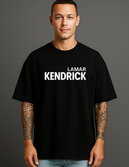 Young man in ATRAYE black streetwear T-shirt with 'Lamar Kendrick' print, tattooed arms.