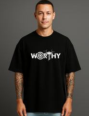 Man in black ATRAYE streetwear T-shirt with bold 'WORTHY' graphic and tattooed arms
